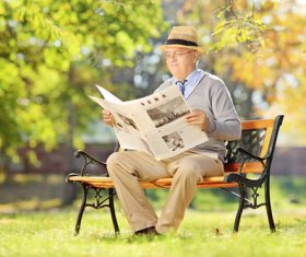 Senior man sitting on park bench reading newspaper Stock Photo