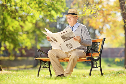 Senior man sitting on park bench reading newspaper Stock Photo