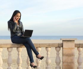 Stock Photo Girl using laptop while answering the phone