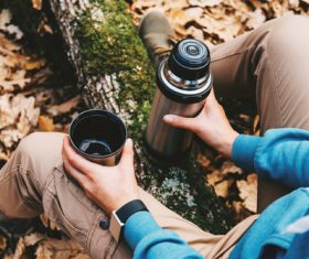 Stock Photo Man sitting on tree trunk holding thermos mug