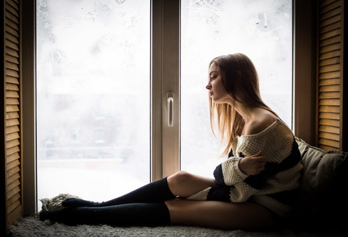 Unhappy girl sitting at the window Stock Photo