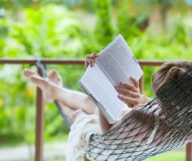 Woman lying in hammock reading book Stock Photo