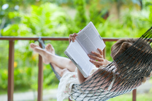 Woman lying in hammock reading book Stock Photo