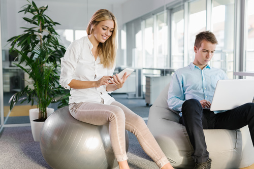Woman sitting on fitness ball looking at mobile phone Stock Photo
