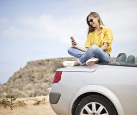 Girl sitting on the top of the car looks at the phone Stock Photo