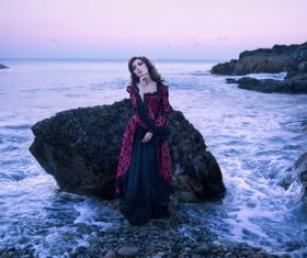 Woman standing next to rock by the sea Stock Photo