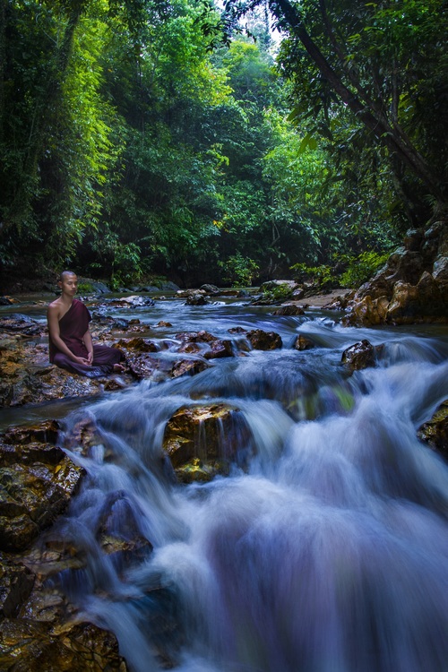 Monk sitting next to the stream meditating Stock Photo