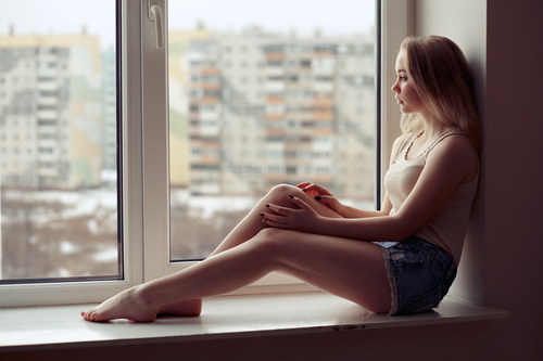 Stock Photo Girl sitting on the window sill and looking out the window