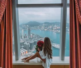 Stock Photo Girl sitting on the window sill holding rose