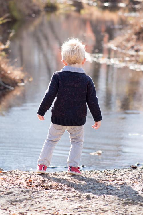 Little boy looking at the fallen leaves in the river Stock Photo