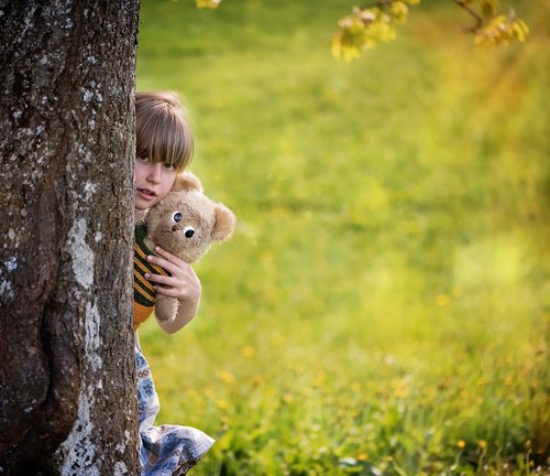 Little girl hugging teddy bear hiding behind tree Stock Photo