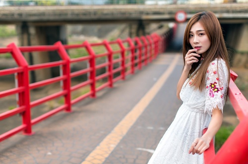 Asian woman in white dress leans on the road railing to take photo Stock Photo