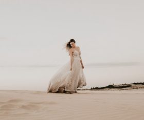 Woman in white dress walks on the beach Stock Photo