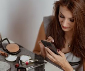 Woman preparing makeup looking at mobile phone Stock   Photo