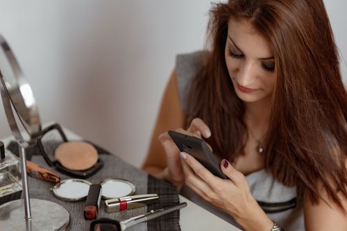 Woman preparing makeup looking at mobile phone Stock   Photo