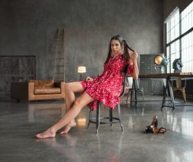 Woman wearing red floral dress doing pose on an indoor chair Stock Photo 02