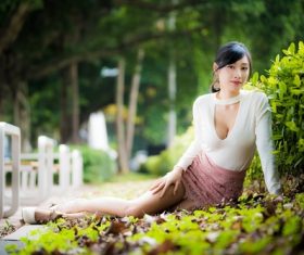 Asian woman posing in city park leaning against plants Stock Photo