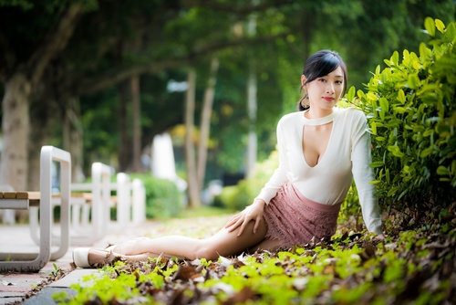 Asian woman posing in city park leaning against plants Stock Photo