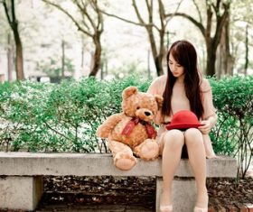 Girl and teddy bear sitting on outdoor stone bench Stock Photo