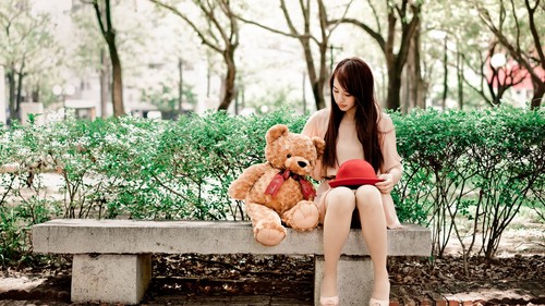 Girl and teddy bear sitting on outdoor stone bench Stock Photo