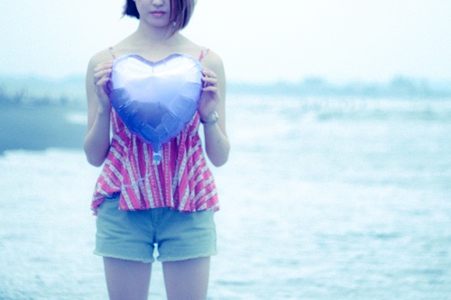 Girl holding heart shaped balloon by the sea Stock Photo