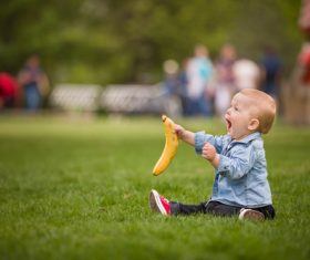 Little boy sitting on the grass holding banana Stock Photo