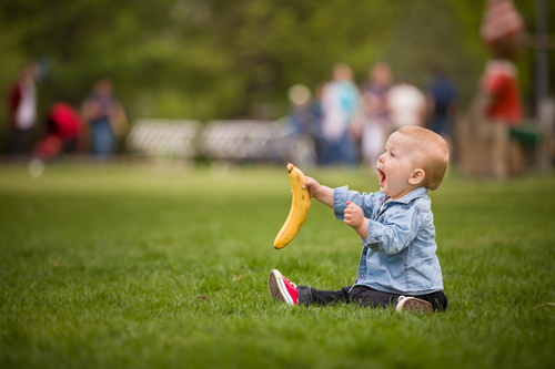 Little boy sitting on the grass holding banana Stock Photo