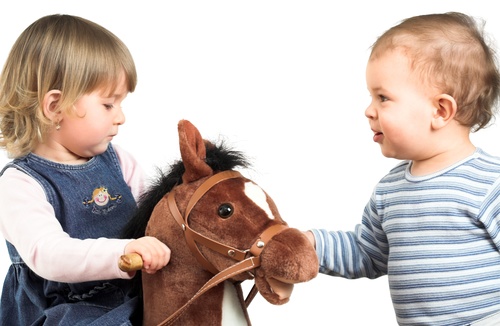 Little girl and little boy riding wooden horse Stock Photo
