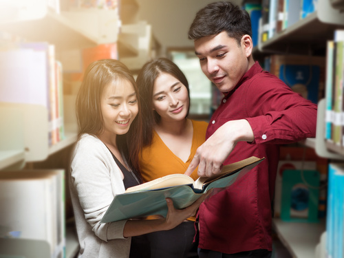 Male and female college students reading books in the library Stock Photo