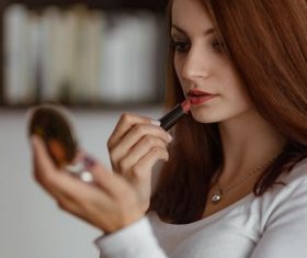 Woman applying lipstick to small mirror Stock Photo