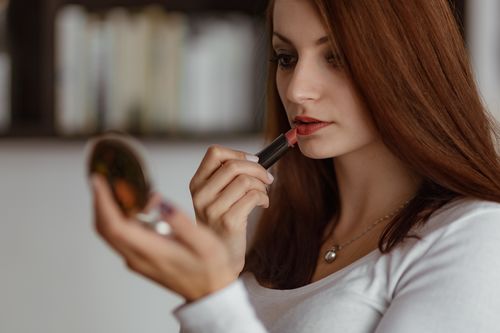 Woman applying lipstick to small mirror Stock Photo