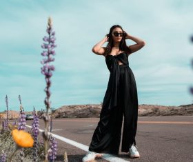 Woman in black long dress standing beside tar road Stock Photo