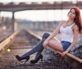 Woman in white vest with denim shorts sits on train tracks Stock Photo