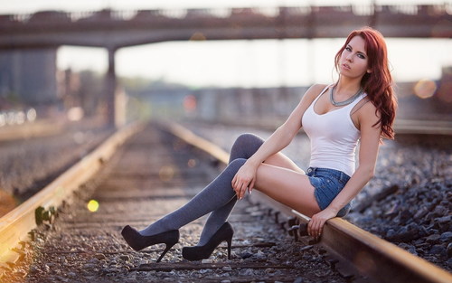 Woman in white vest with denim shorts sits on train tracks Stock Photo