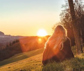 Woman sitting on the hillside looking at the rising sun Stock Photo
