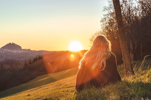 Woman sitting on the hillside looking at the rising sun Stock Photo