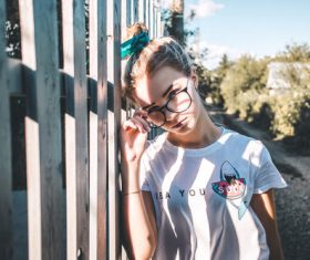 Young girl with glasses leans on the fence Stock Photo