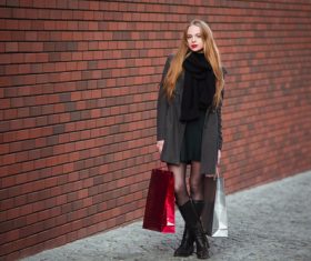 Young woman standing in front of red wall holding shopping bags Stock Photo 01