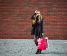Young woman standing in front of red wall holding shopping bags Stock Photo 02