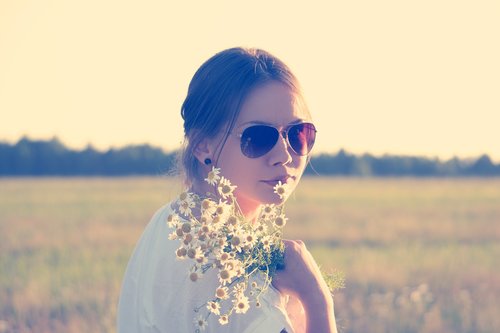 young woman wearing sunglasses and holding wildflowers in meadow Stock Photo