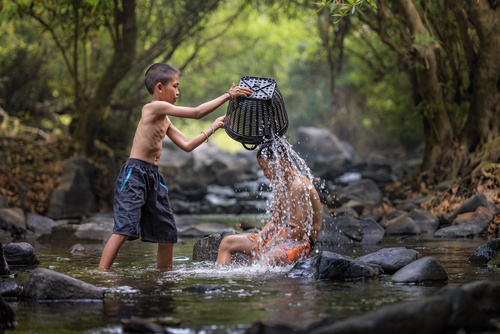 Children in the river holding bamboo baskets splashing water Stock Photo