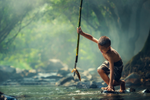 Little boy catching fish with harpoon in the river Stock Photo