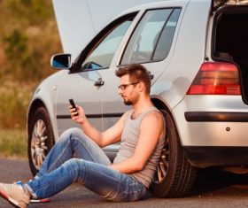 Man sitting next to the car and looking at the phone Stock Photo
