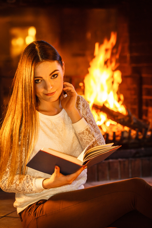 Woman reading a book by the fireplace Stock Photo