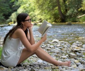 Woman reading book by the stream Stock Photo
