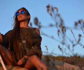 Woman wearing sunglasses holding wooden stick sitting on the desert Stock Photo